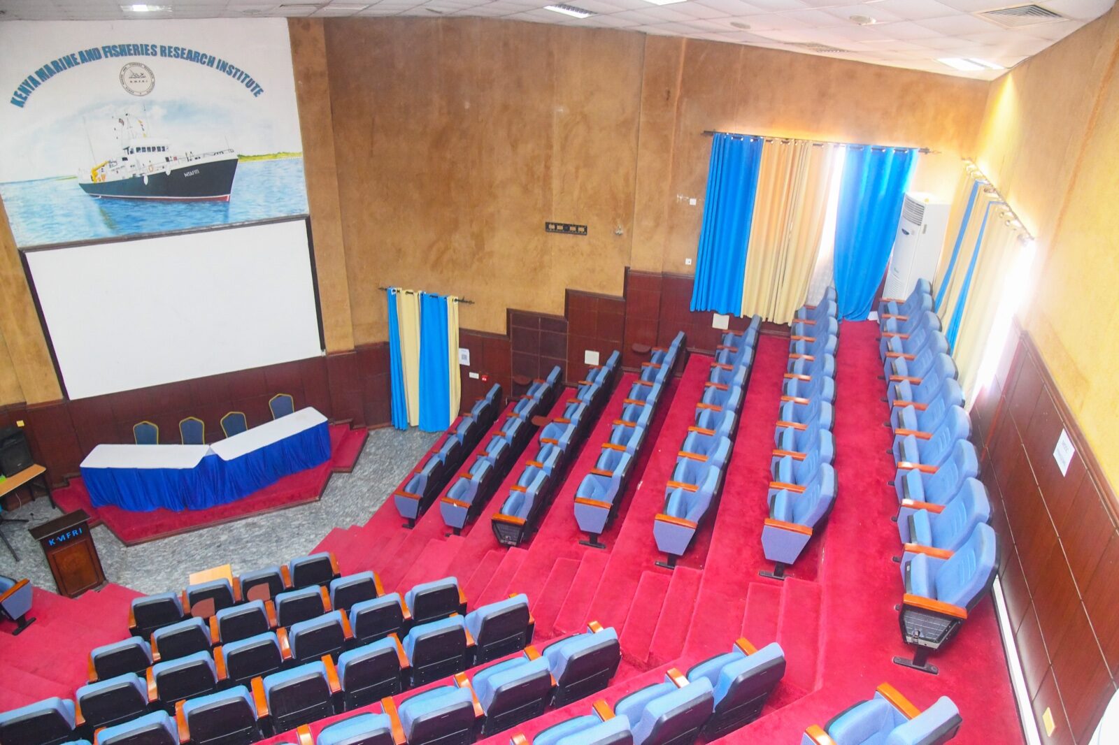 Main Auditorium stage, projector screen and KMFRI research-vessel mural